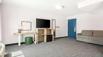 A modern room with a flat-screen TV, a desk with a computer, a green trash bin, a sofa, and a blue door.