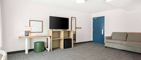 A modern room with a flat-screen TV, a desk with a computer, a green trash bin, a sofa, and a blue door.