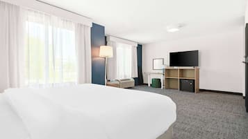 Una habitación de hotel con una cama grande, un escritorio con silla, un televisor y un mueble pequeño.