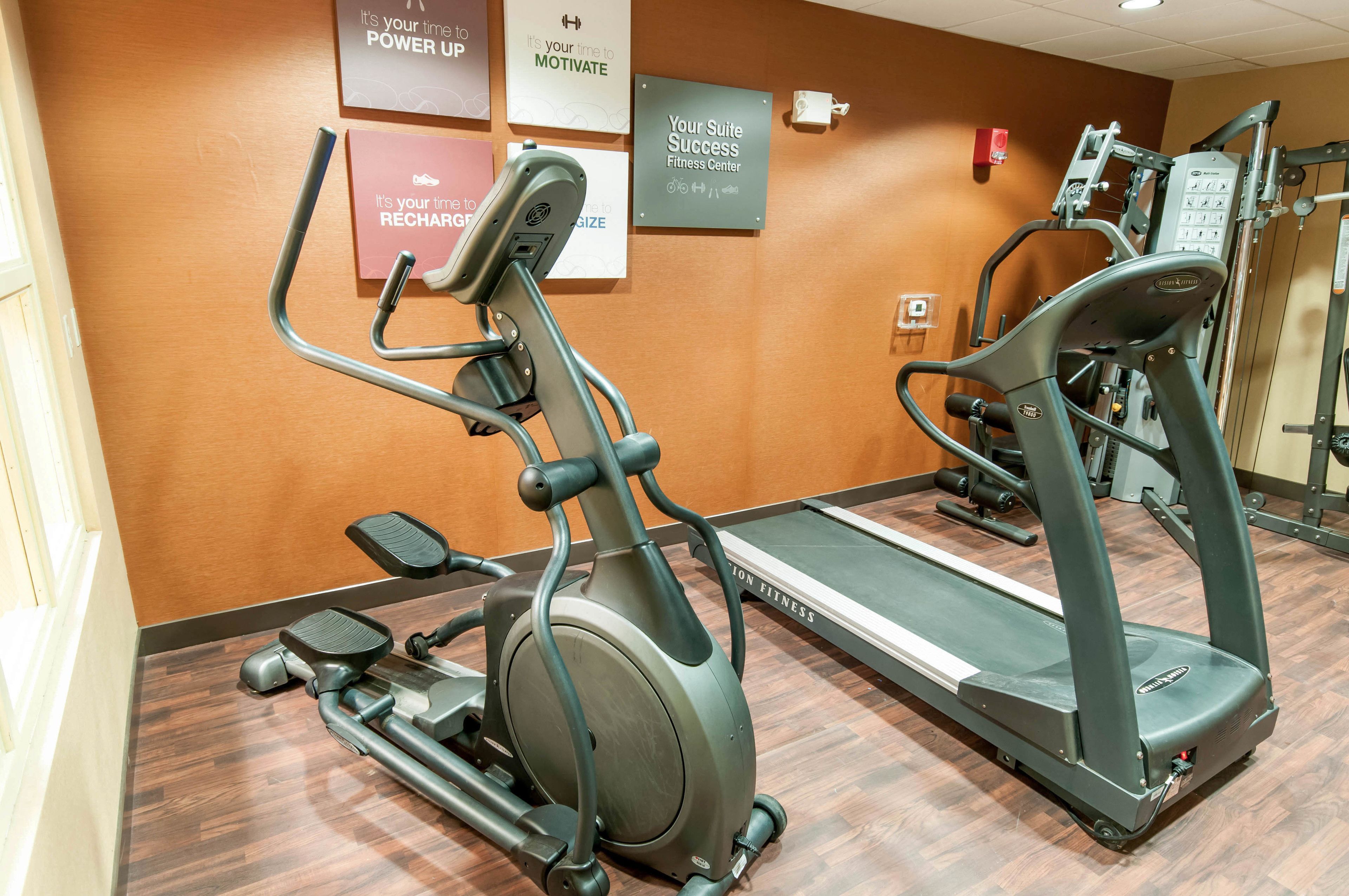 Un gimnasio con cintas de correr, elípticas y carteles motivacionales en la pared.