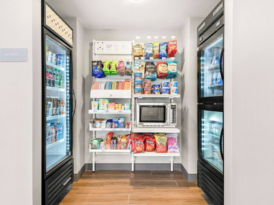 Una kitchenette pequeña y bien organizada, con microondas, refrigerador y estantes llenos de refrigerios y bebidas.