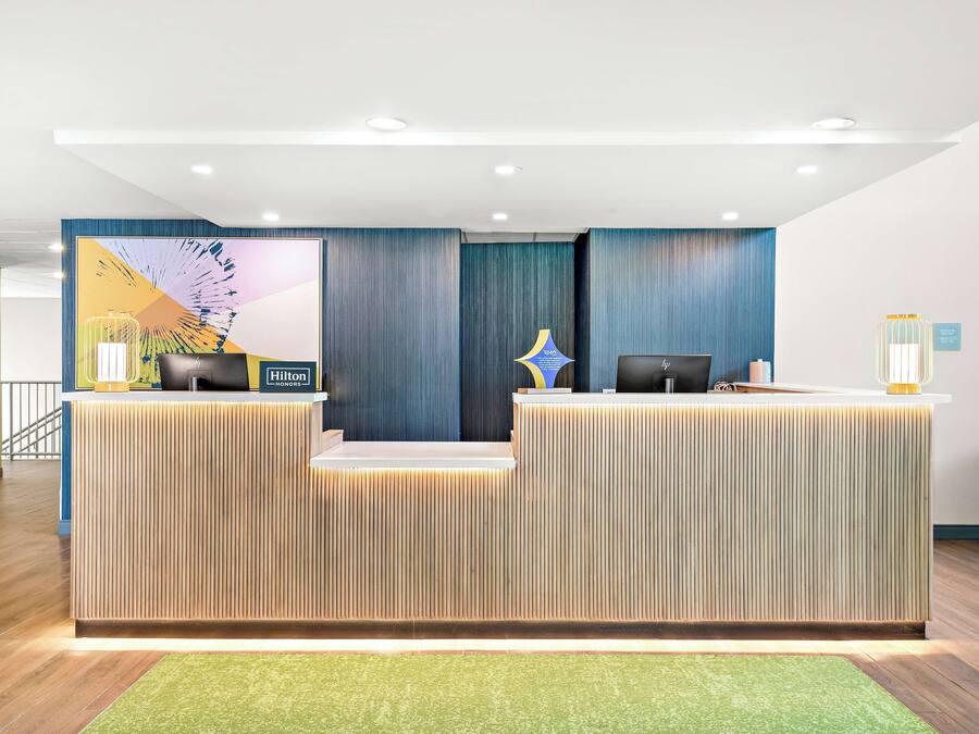 A modern hotel reception desk with a vertical wood panel design, a digital screen, and a reception counter.