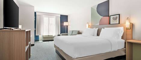 A hotel room with a large bed, a flat-screen TV, a desk, and a window with curtains.
