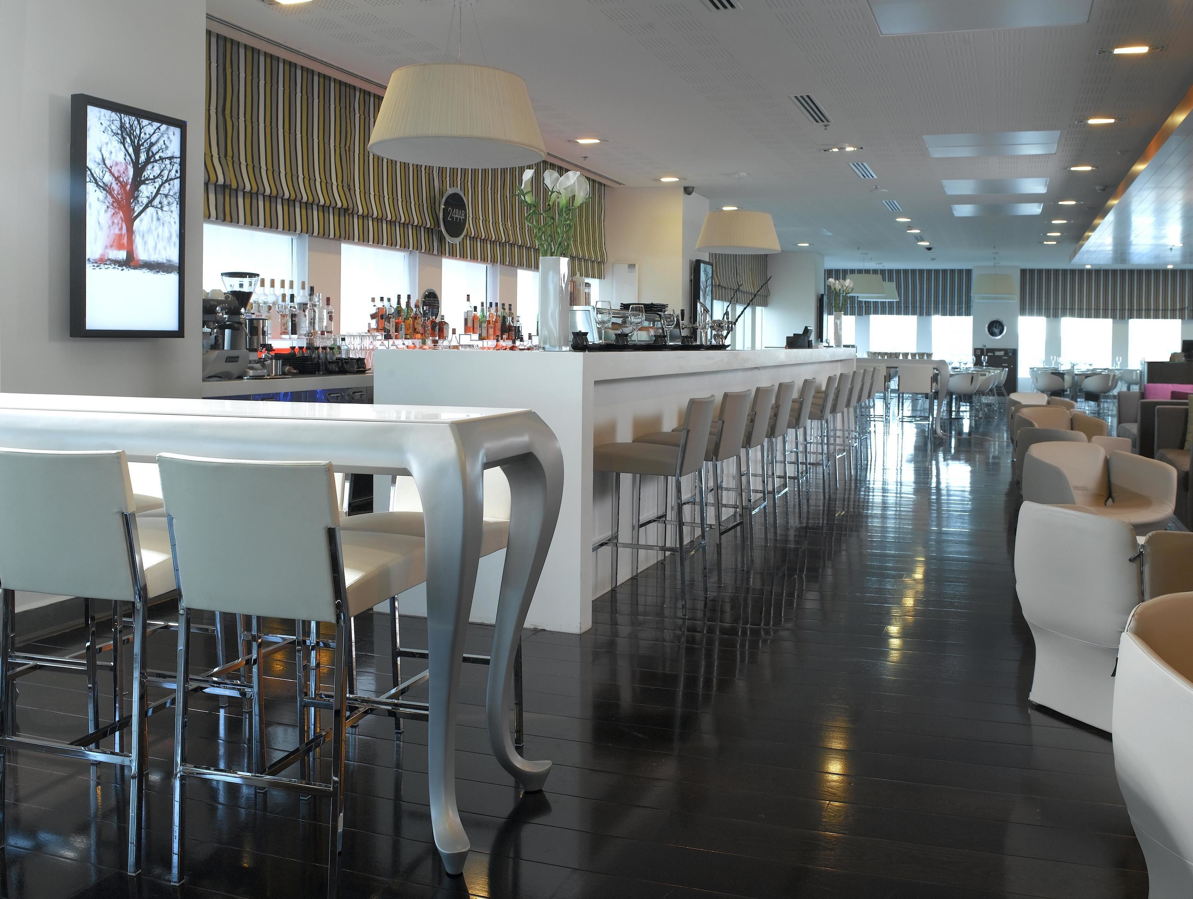 A modern bar area with a long counter, multiple bar stools, and a seating area with chairs.