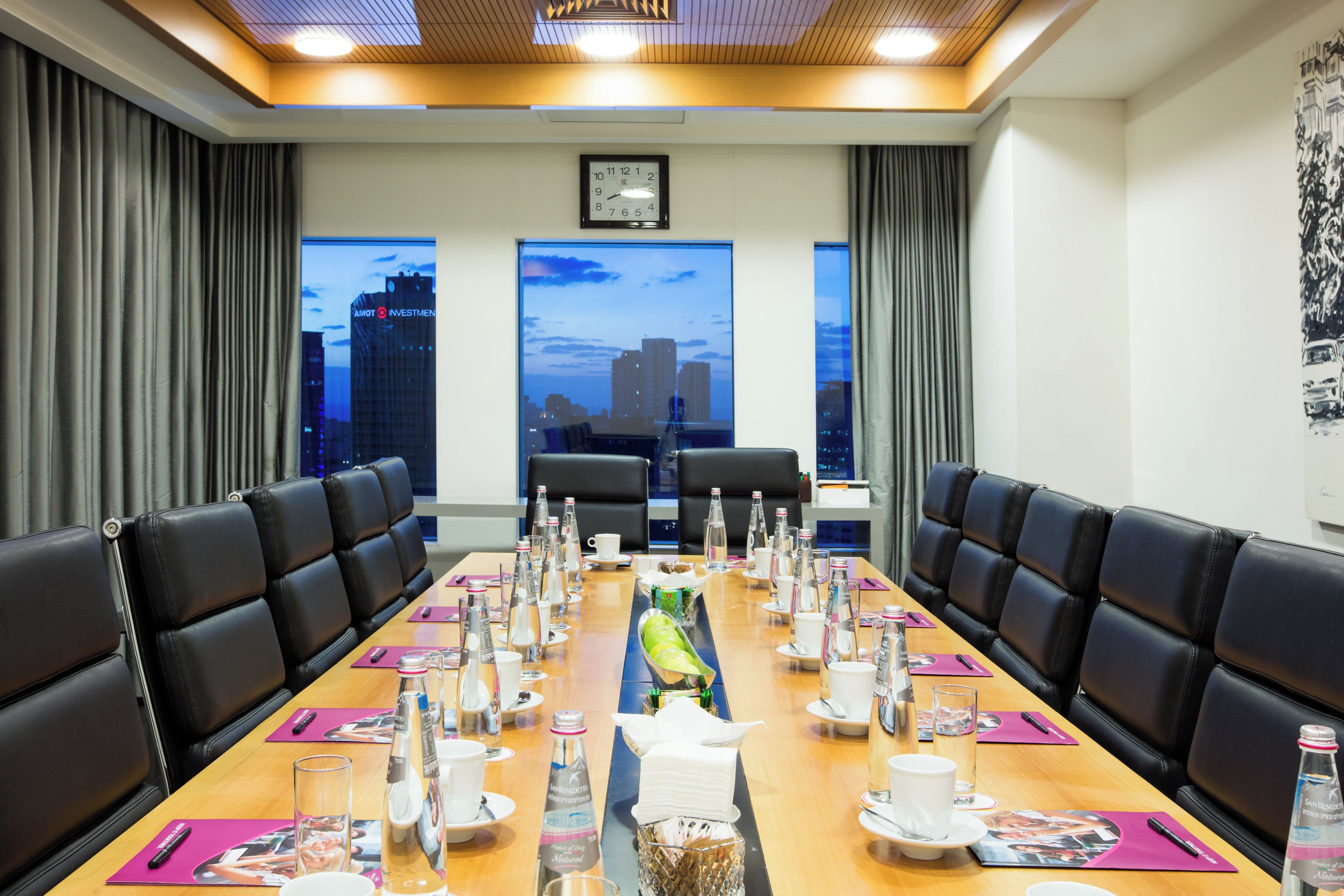 A conference room with a long table, black leather chairs, and a cityscape view through large windows.