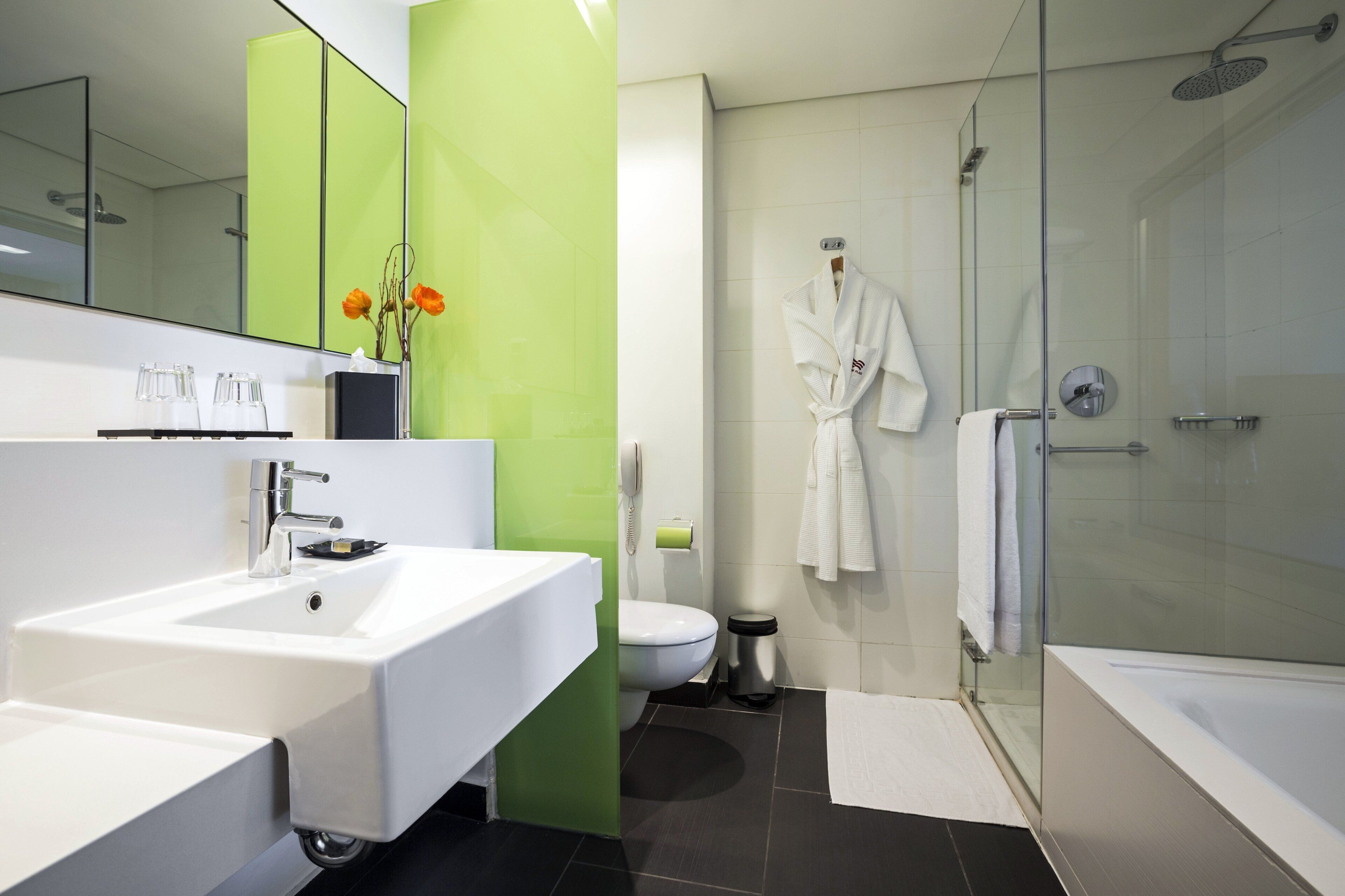 A modern bathroom with a white sink, a glass shower enclosure, and a green accent wall.