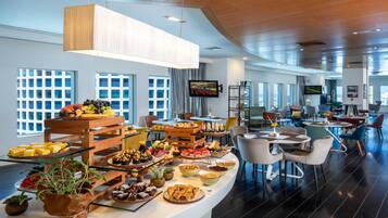 A modern hotel lobby with a buffet area featuring various food items and a seating area with comfortable chairs and tables.