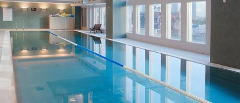 A large indoor swimming pool with clear water, surrounded by windows and a seating area.