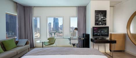 A modern hotel room with a large bed, a desk, a chair, and a television.