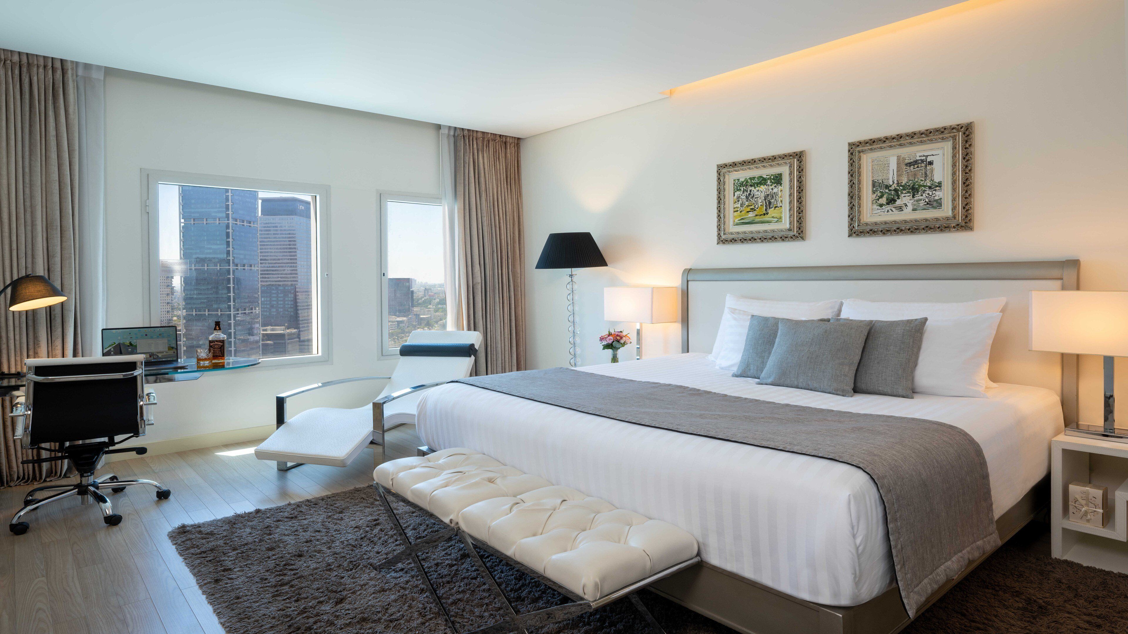 A modern hotel room with a large bed, a desk, a chair, and a view of the city.