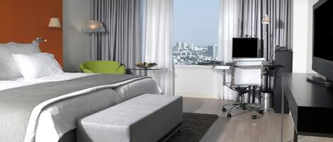 Una habitación de hotel moderna con una cama grande, un escritorio, una silla, un televisor y vistas de la ciudad.