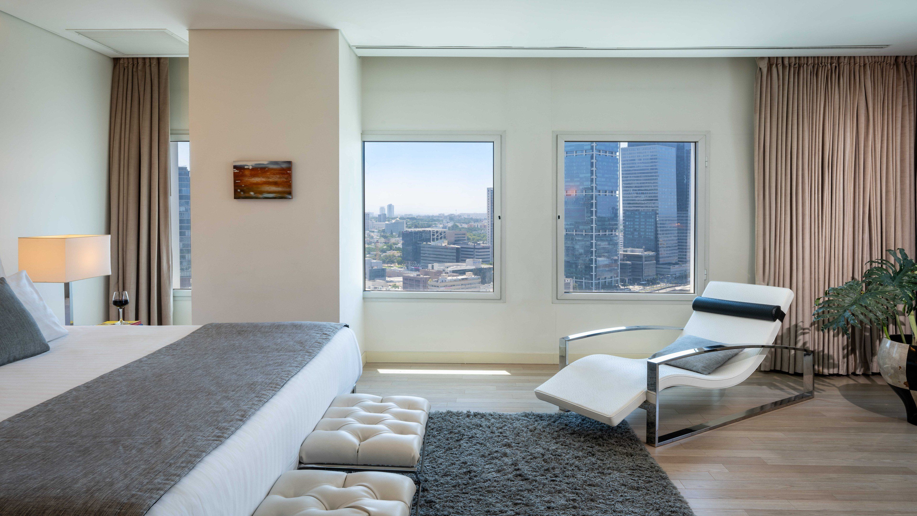 Una habitación de hotel con cama, una silla, vistas a la ciudad y un ventanal con cortinas.