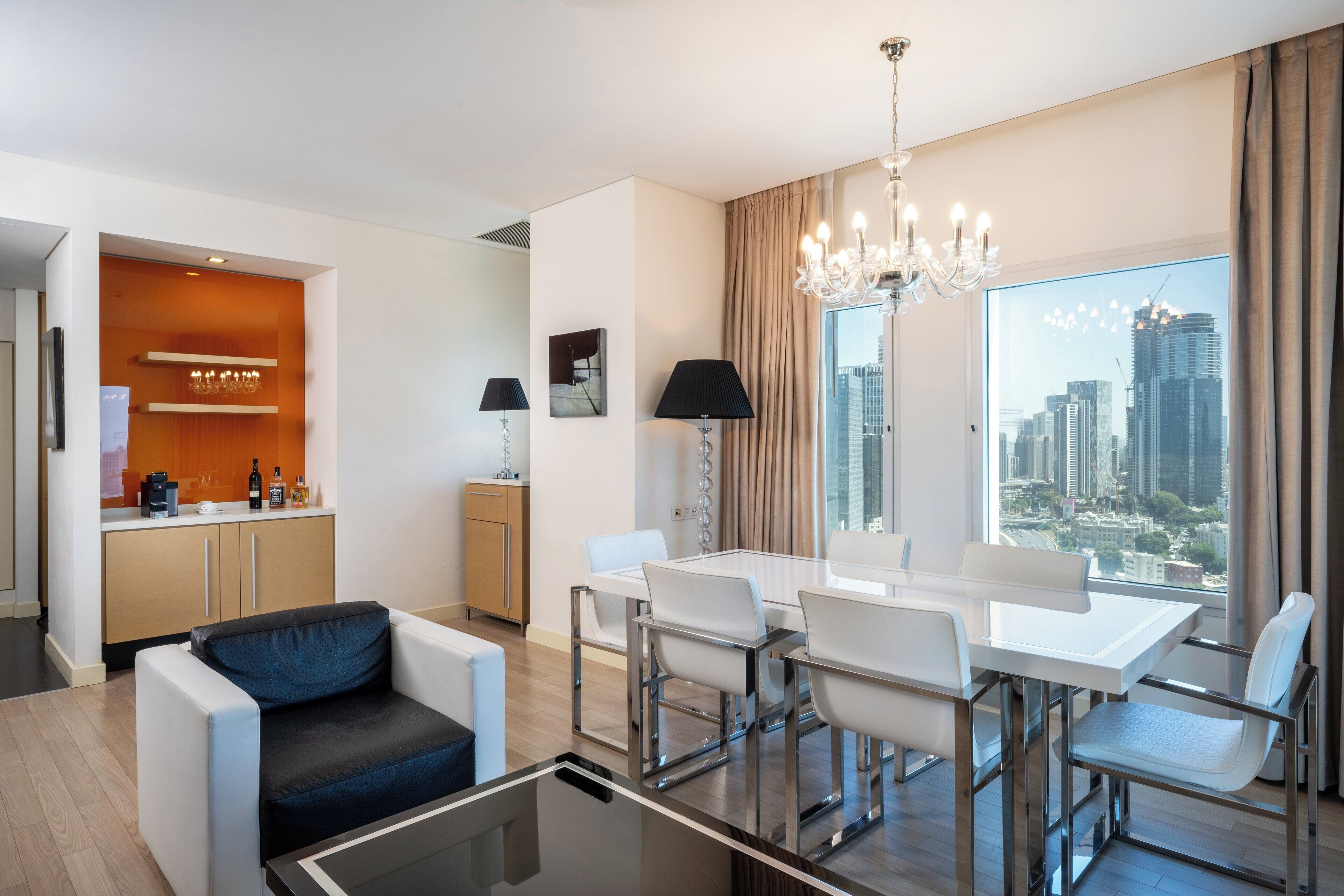 Une chambre d’hôtel moderne dotée d’un coin repas, d’un canapé, d’une machine à café et offrant une vue sur le paysage urbain.