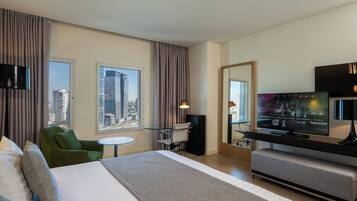 A modern hotel room with a large bed, a desk, a television, and a view of the cityscape.