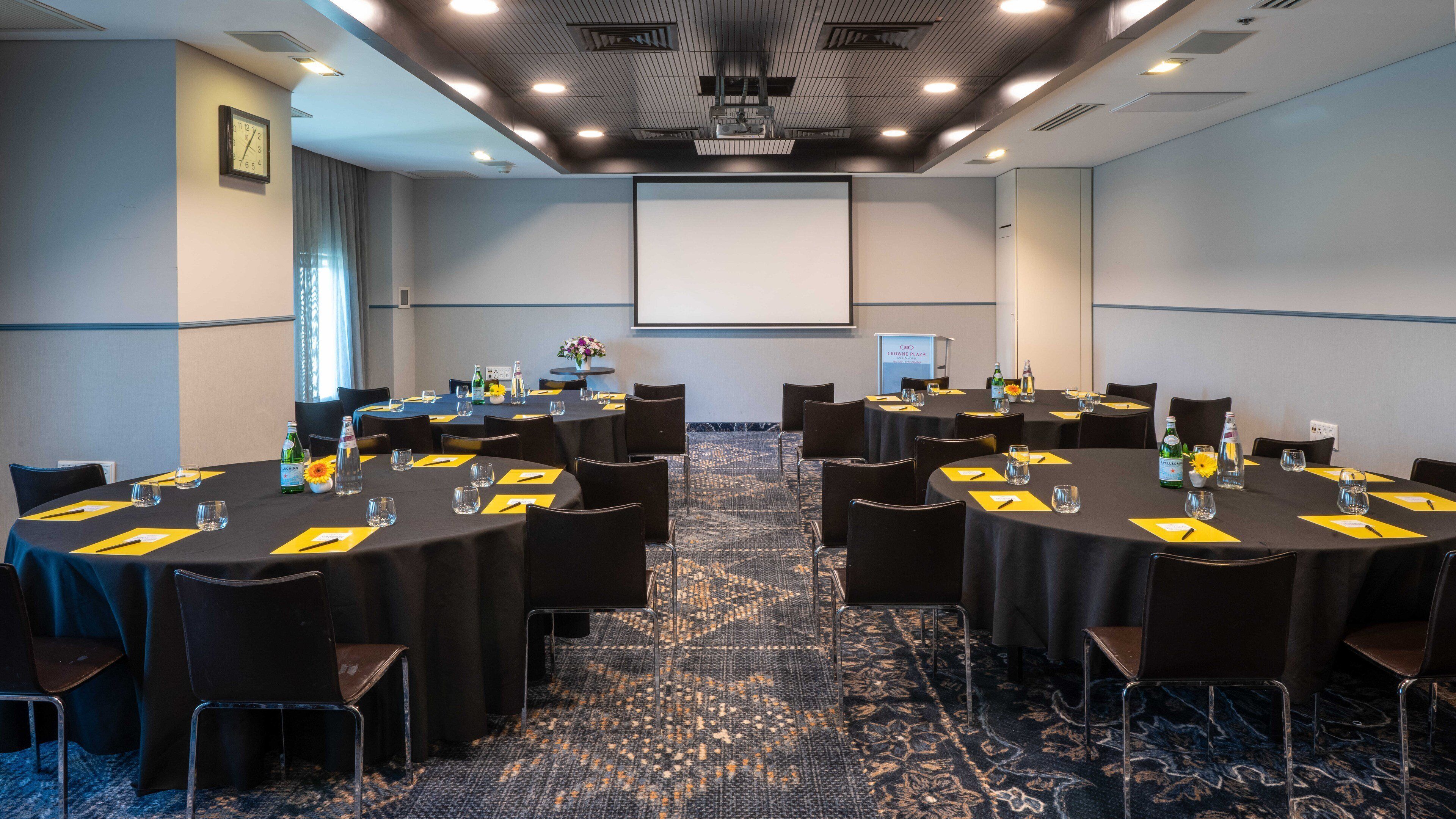 A conference room with multiple tables, chairs, and a projector screen.