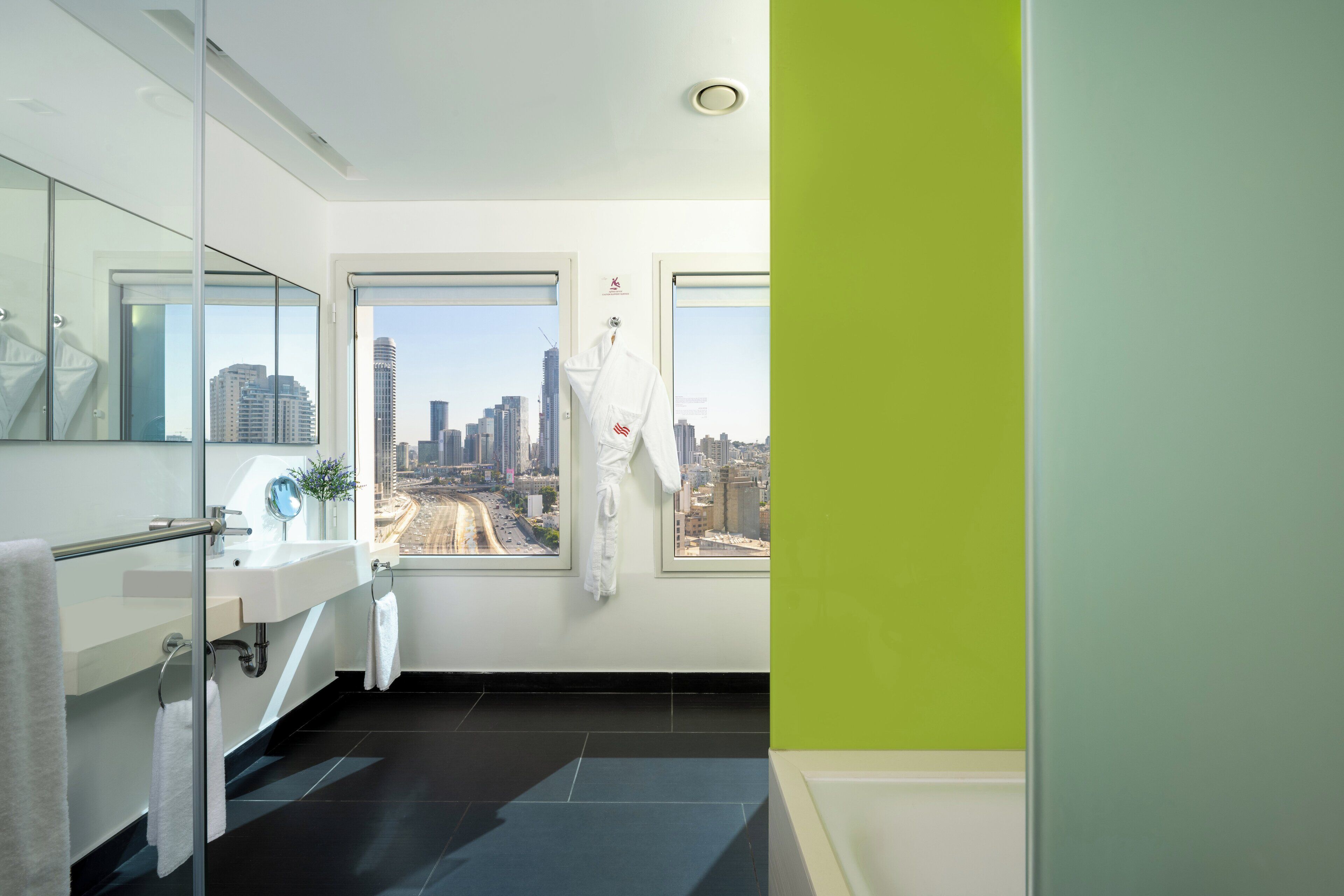 A modern bathroom with a glass partition, a sink, a mirror, and a view of a cityscape through large windows.