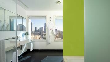 A modern bathroom with a glass partition, a sink, a mirror, and a view of a cityscape through large windows.