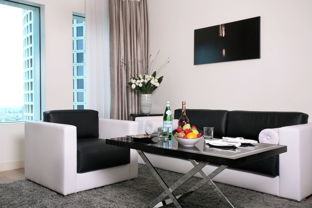 Un salon moderne avec un canapé noir et blanc, une table basse en verre et un panier de fruits.