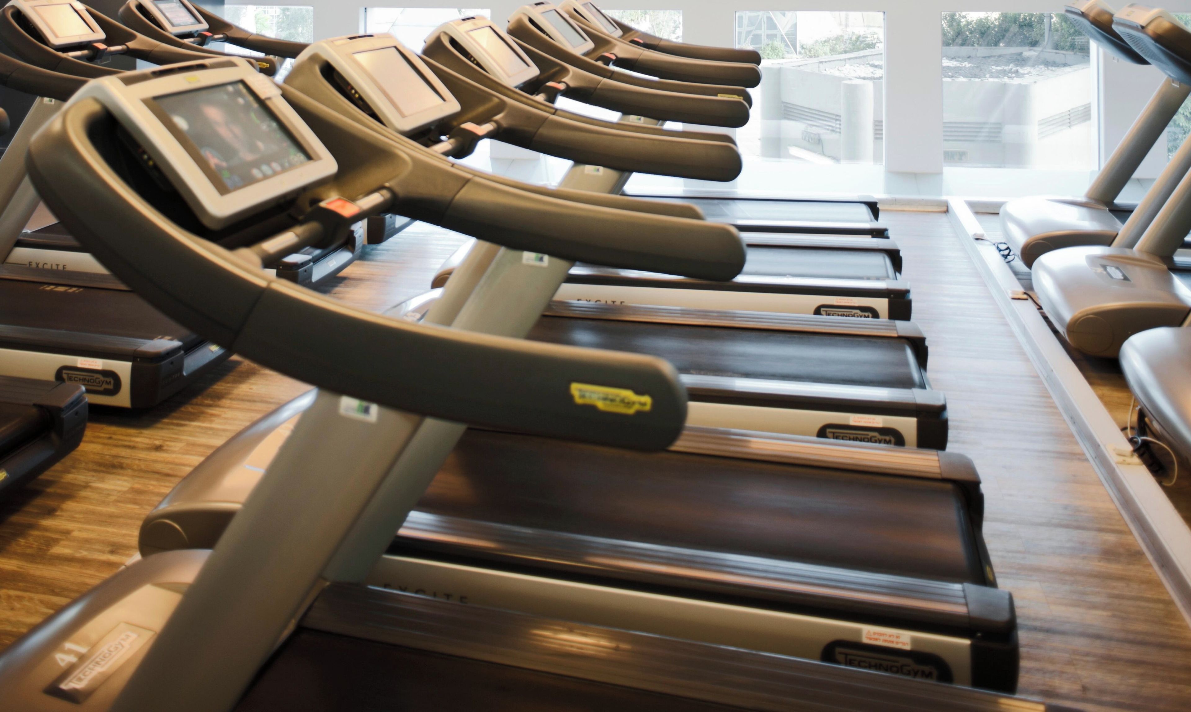 A row of treadmills with digital displays and a wooden floor.