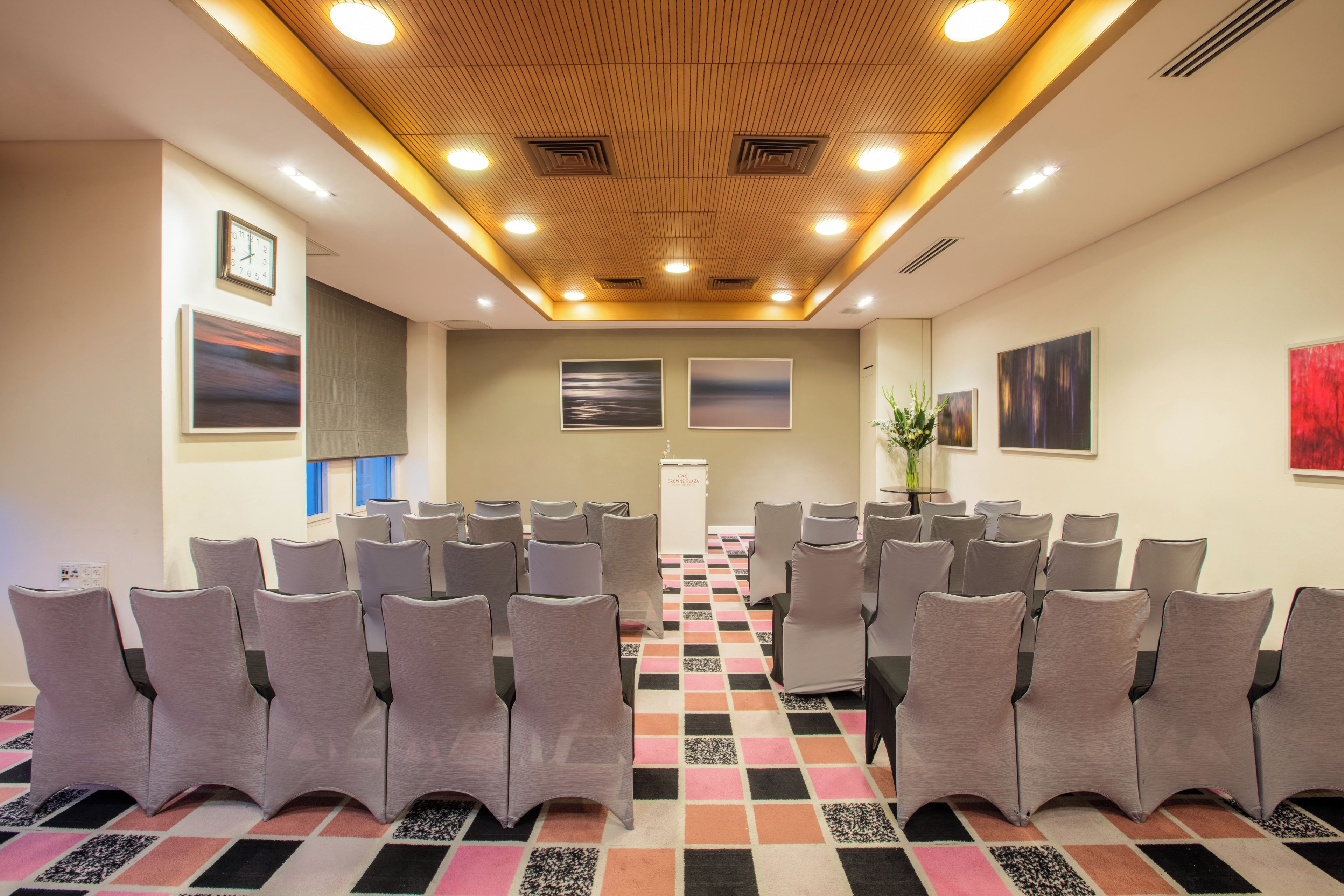Une salle de conférence avec des rangées de chaises, un plafond en bois et des œuvres d’art accrochées aux murs.