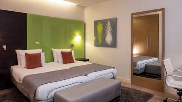 Ett modernt hotellrum med en stor säng, en bänk, ett skrivbord och en stol.