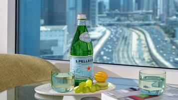 Une bouteille d’eau S. Pellegrino, deux verres et une assiette avec des raisins et un citron, le tout posé sur une table près d’une fenêtre donnant sur la ville.