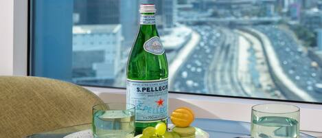 A bottle of S. Pellegrino water, two glasses, and a plate with grapes and a lemon on a table by a window with a city view.