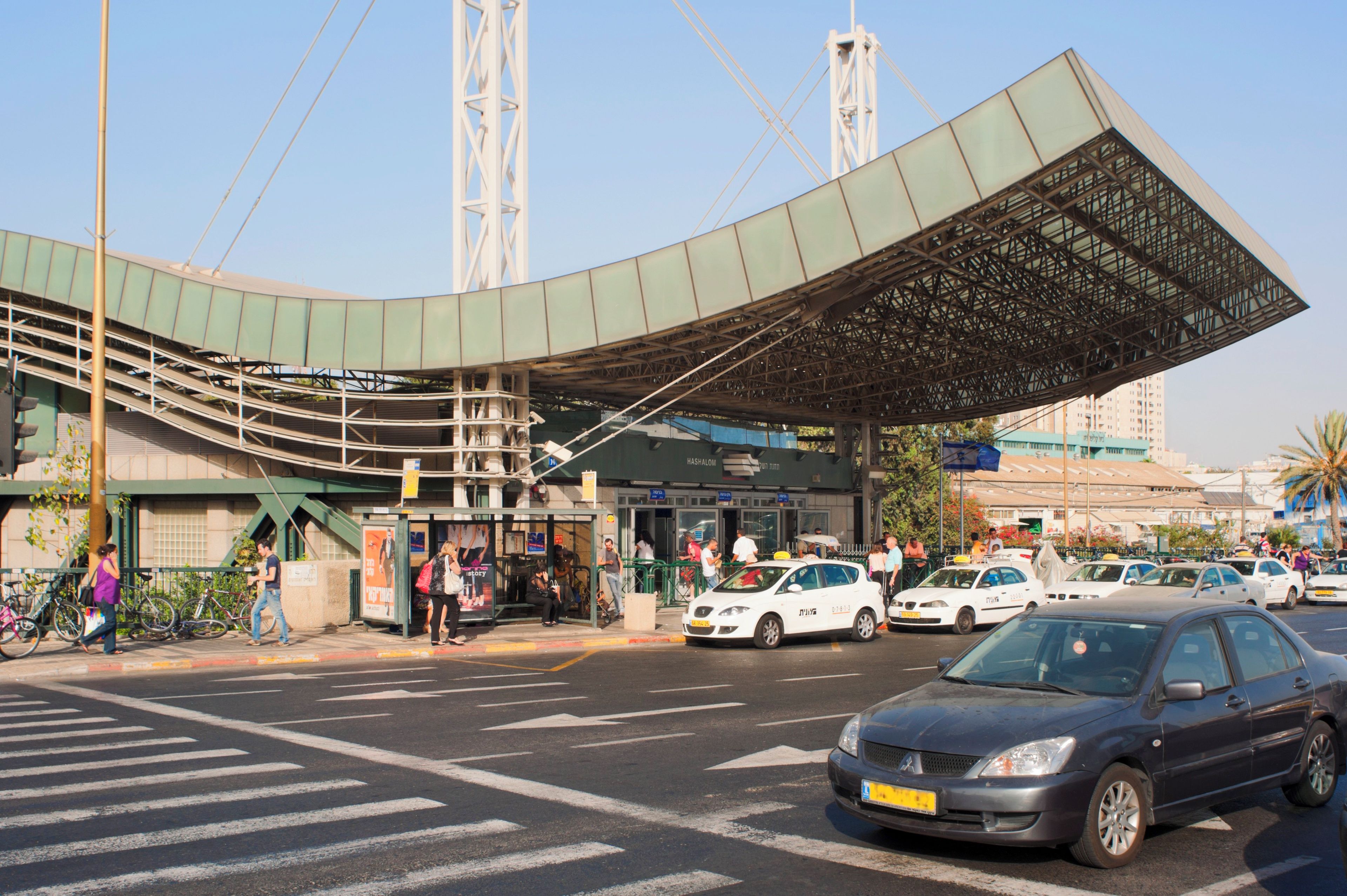 A multi-level parking structure with a curved roof, a pedestrian walkway, and a building with a sign that reads 'HASHALOM'.