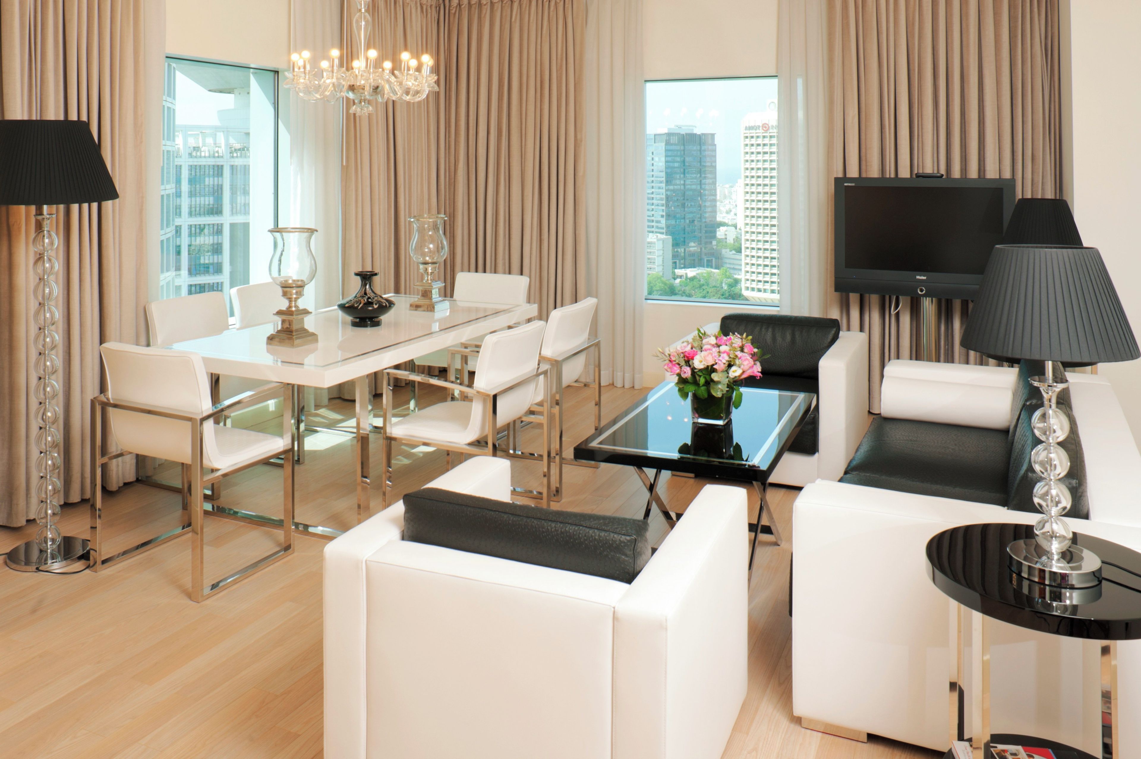 A modern hotel room with a dining area, a sofa, a TV, and a chandelier.