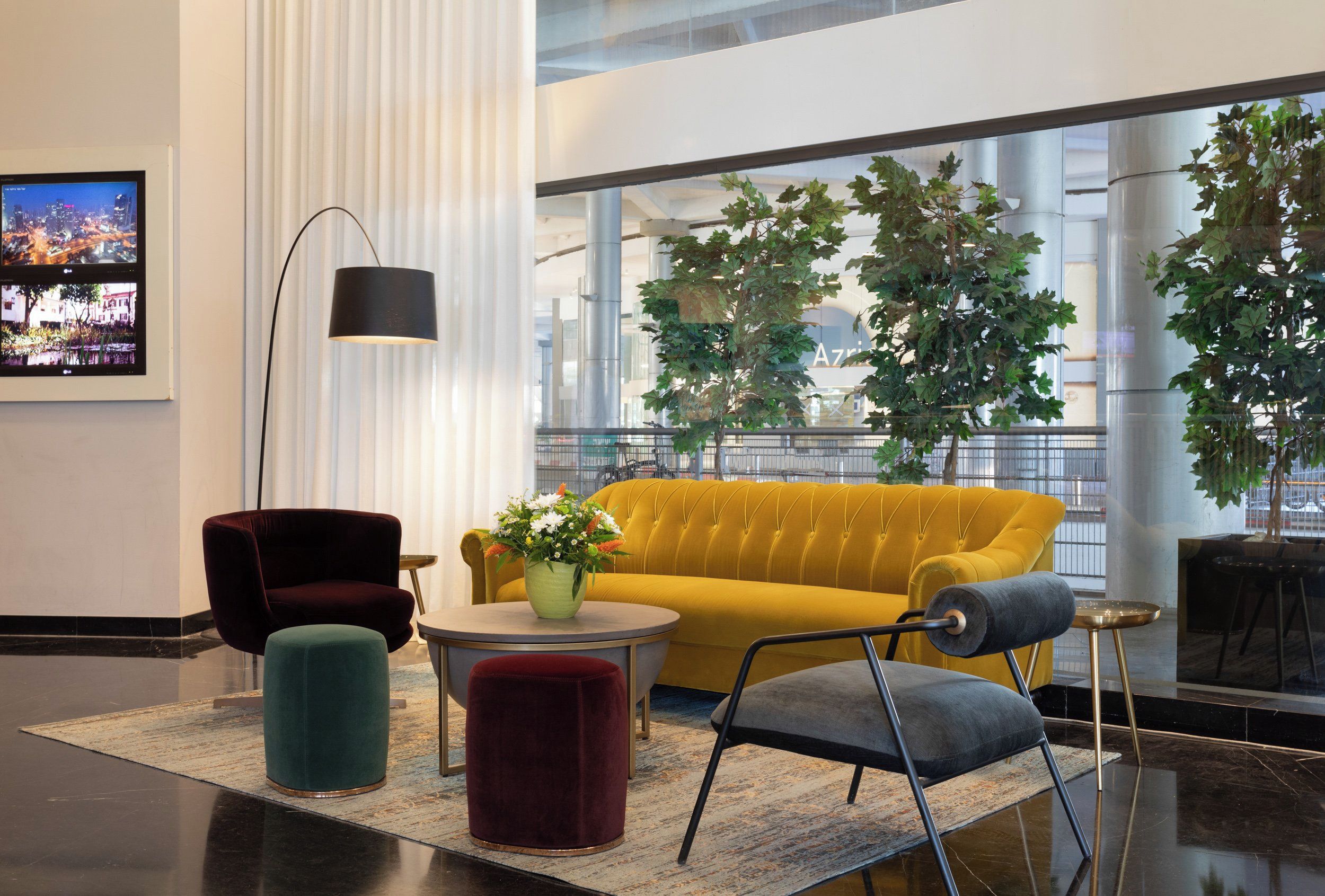 Um hall moderno com um sofá amarelo, uma cadeira vermelha, um banquinho verde e um abajur preto.
