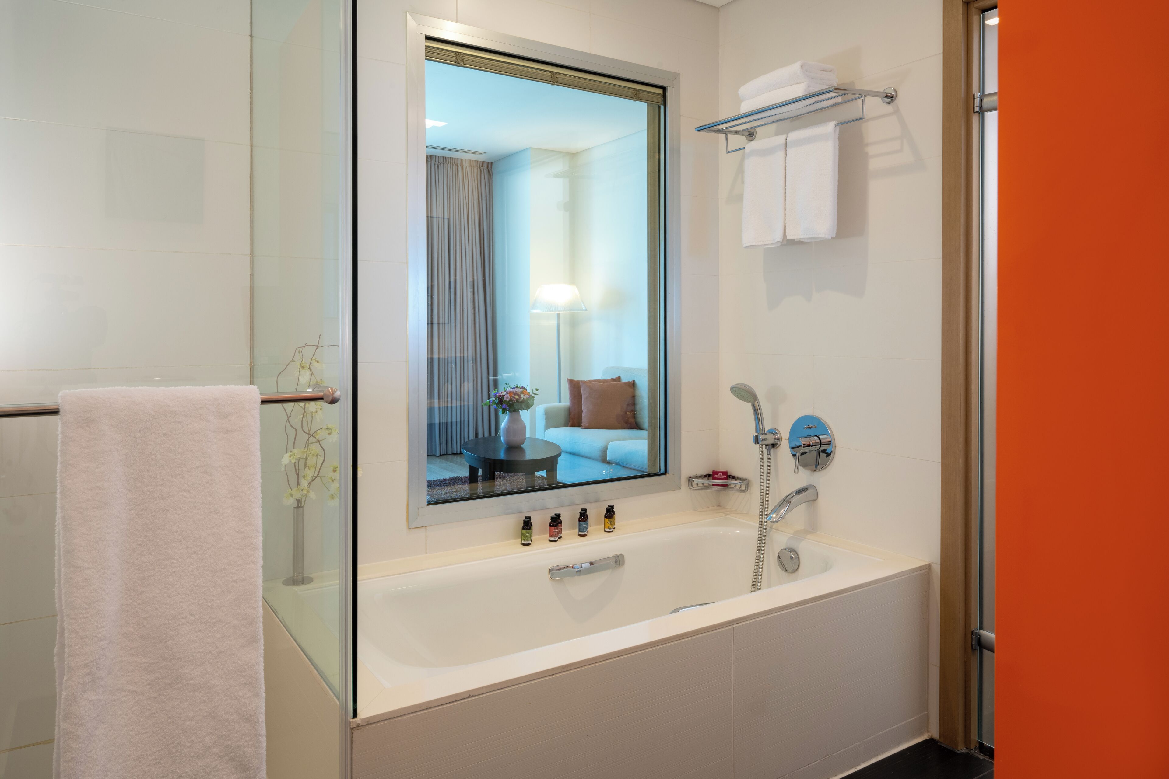 Un baño moderno con un espejo grande, una bañera, una ducha con mampara de vidrio y un perchero para toallas.
