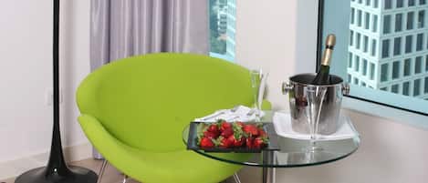Una habitación moderna con una silla verde, una mesa de vidrio y una botella de champán, con vistas a la ciudad a través de una ventana.