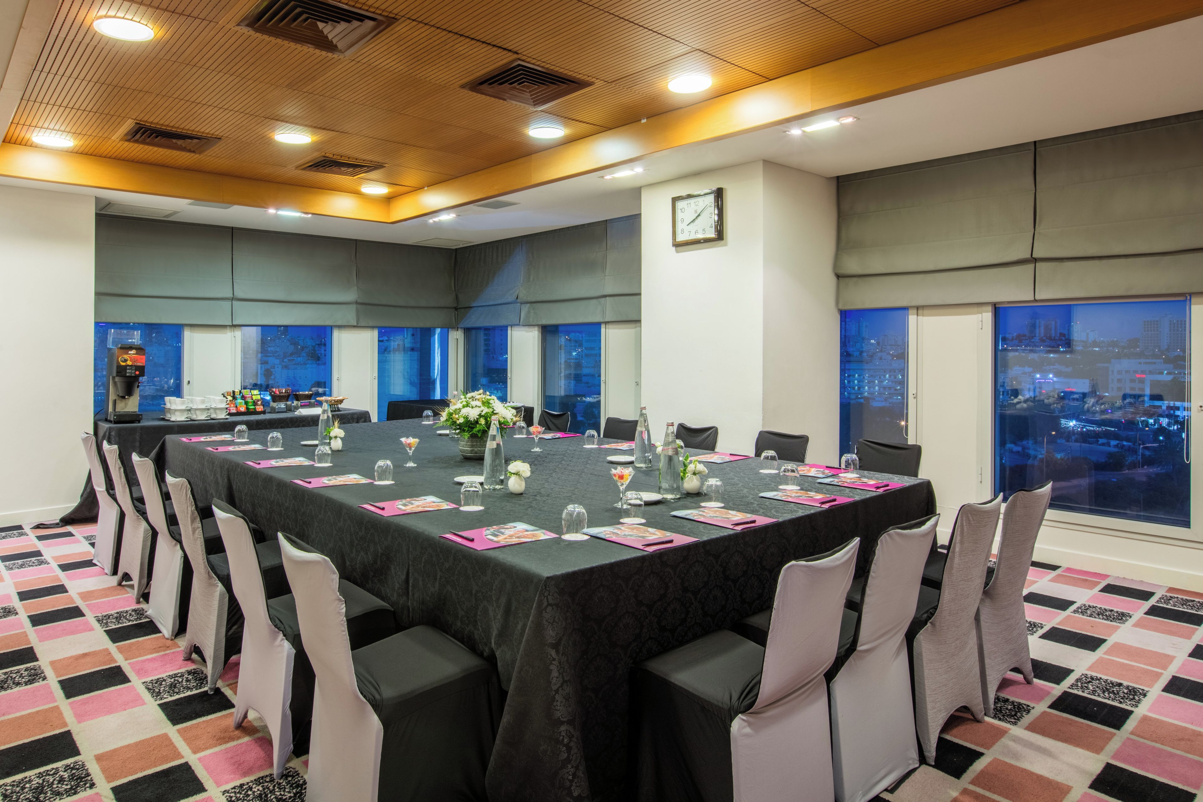 A conference room with a long table, chairs, and a city view through large windows.