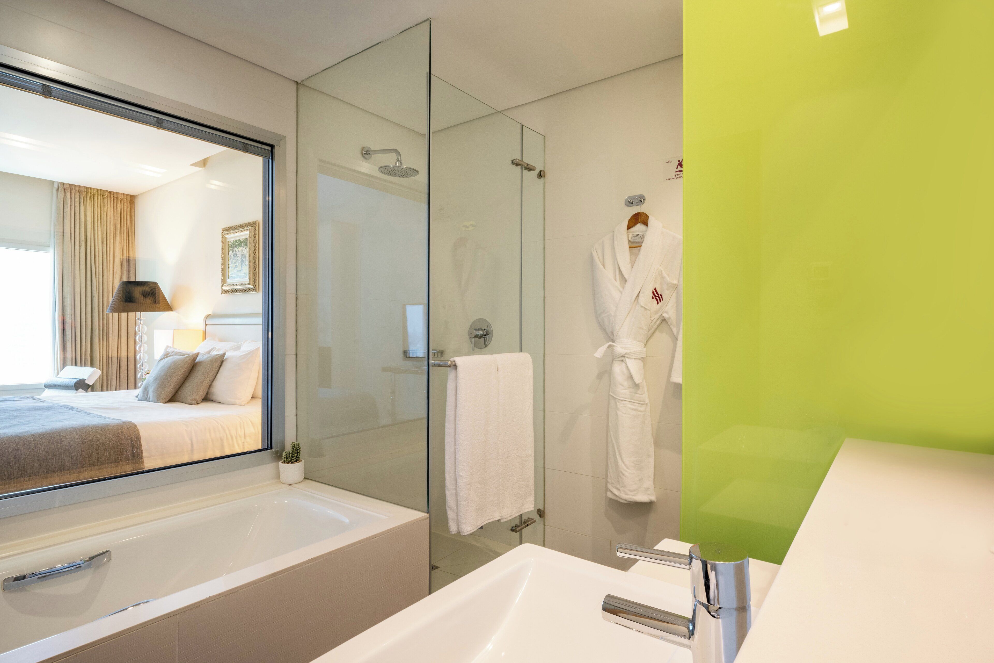 A modern bathroom with a glass shower enclosure, a large bathtub, and a green accent wall.