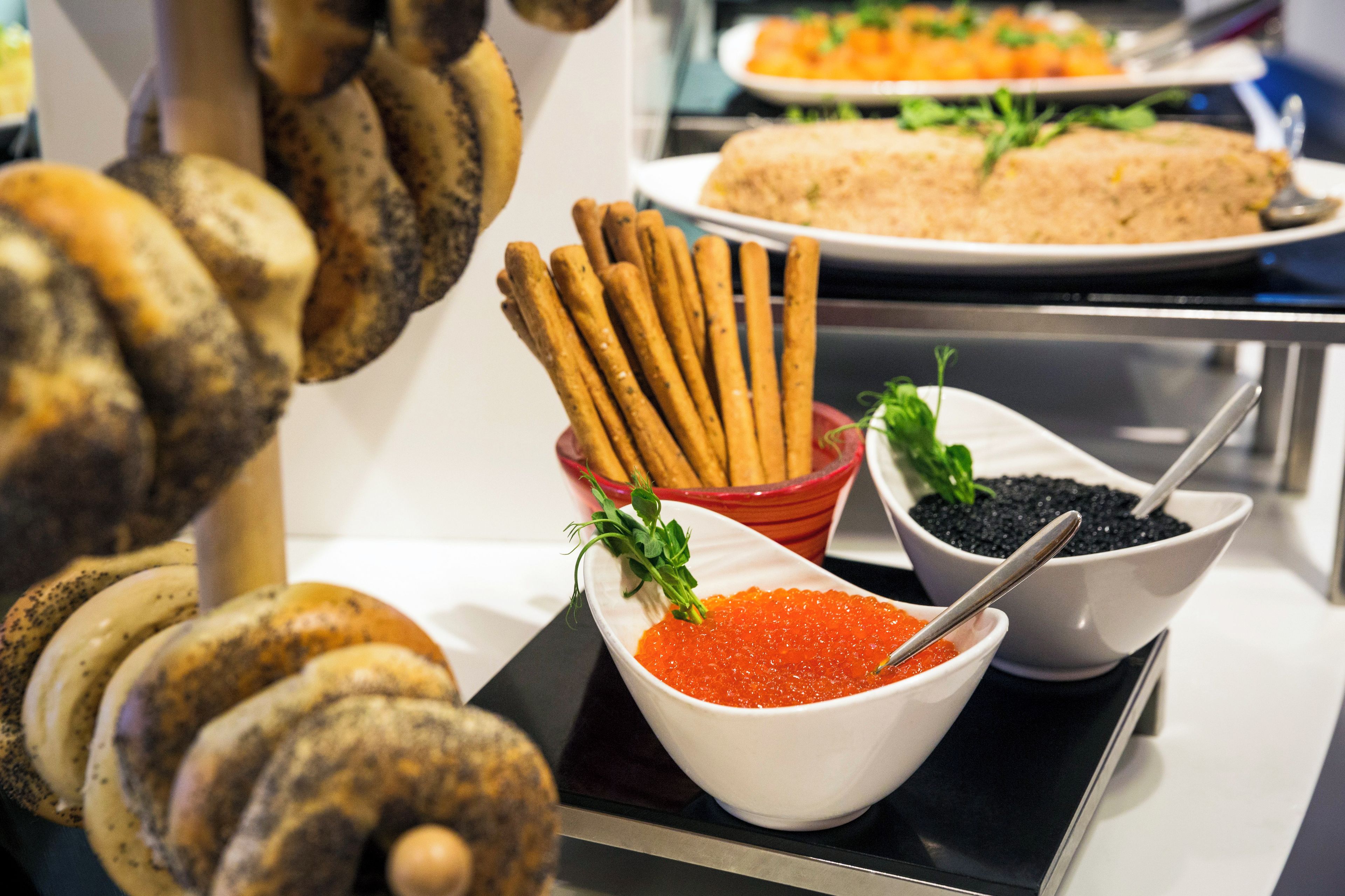 A buffet table with various food items including breadsticks, a bowl of red caviar, and a plate of food.