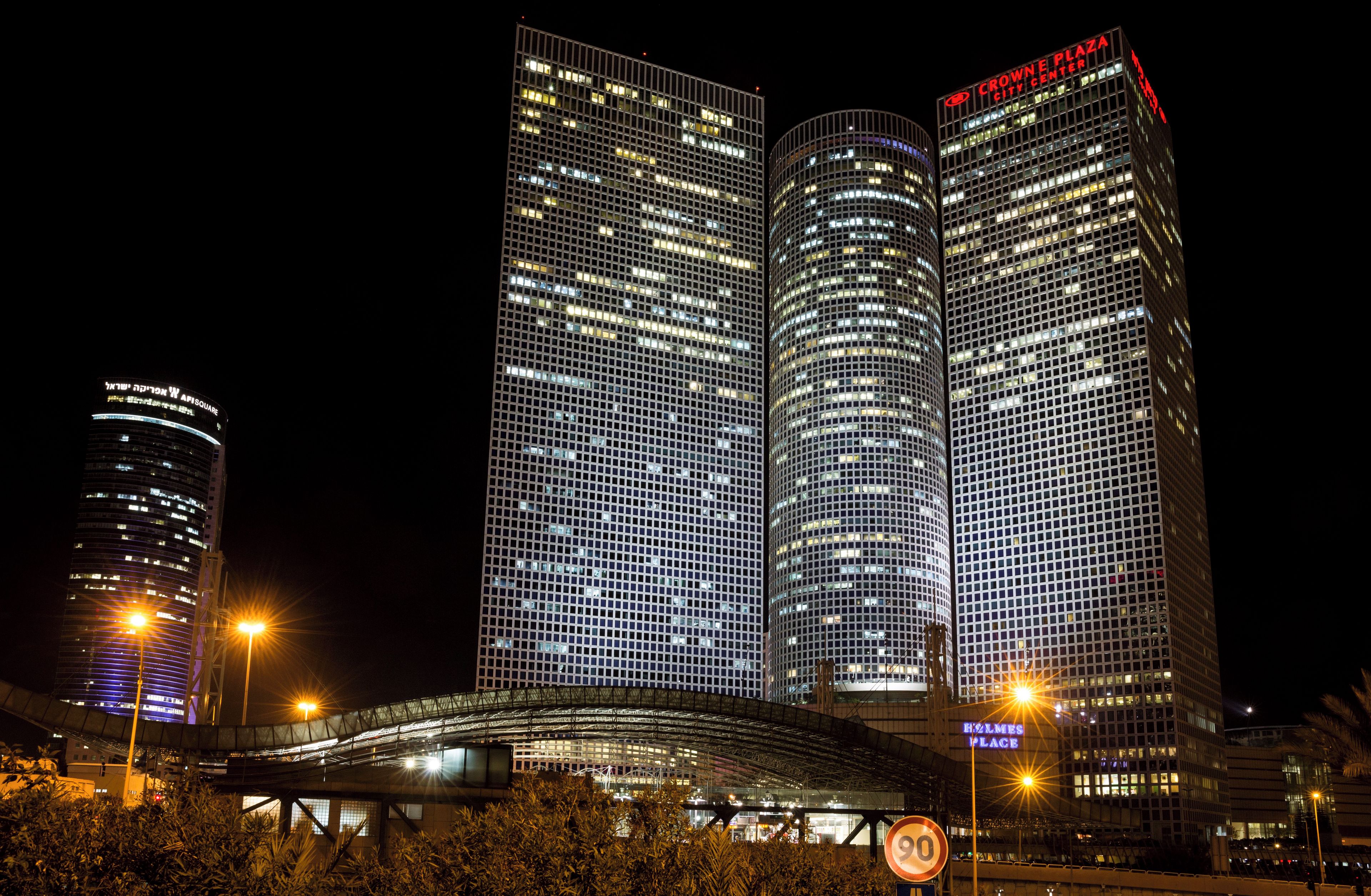 A nighttime view of a cityscape with modern high-rise buildings, including a prominent building with a grid-like facade and illuminated signage.