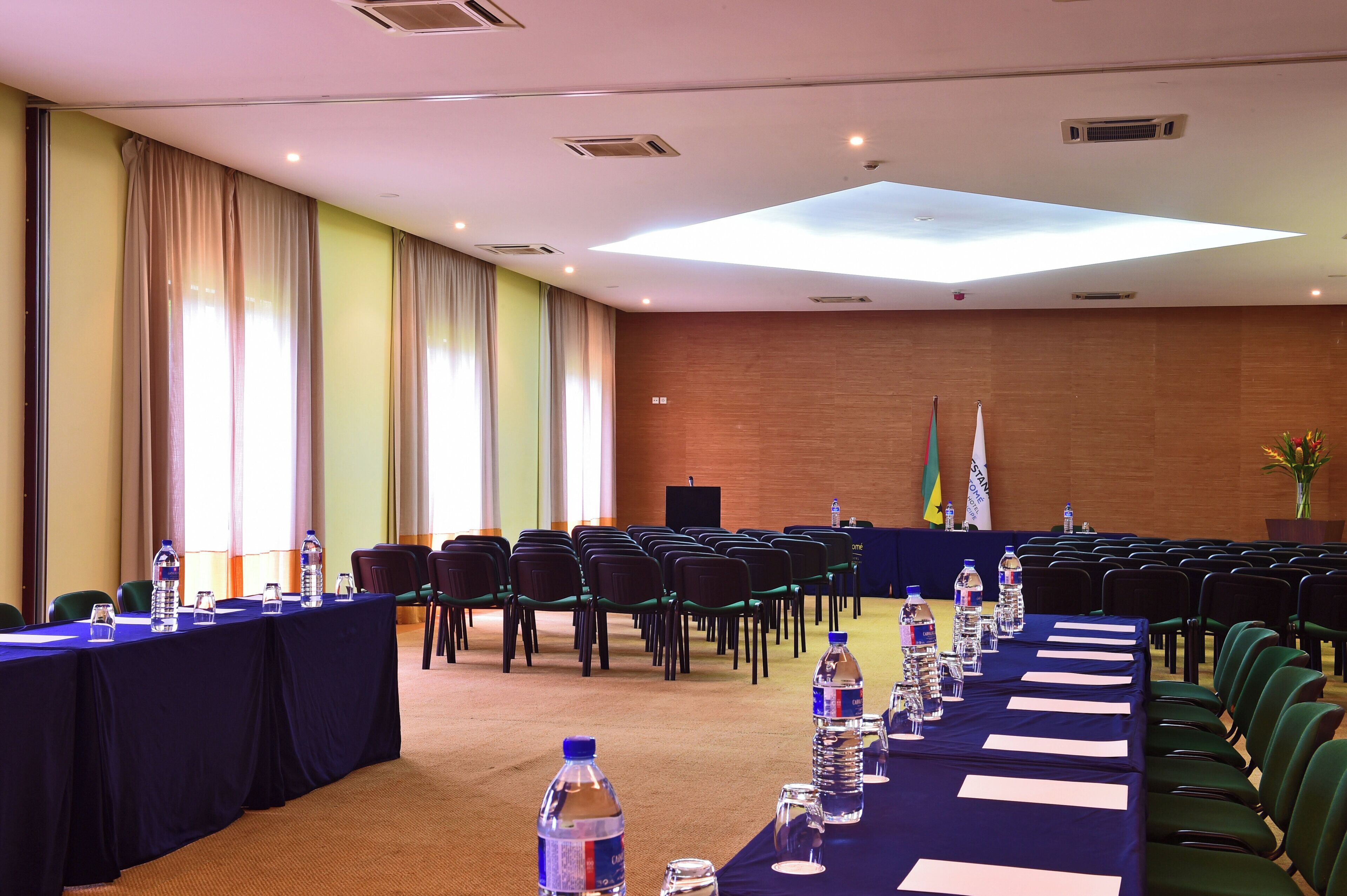 A conference room with rows of chairs, tables with water bottles, and flags.