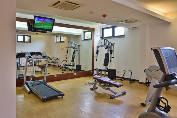 A gym with a treadmill, weight machines, and a mirrored wall.