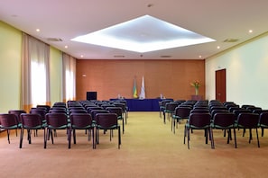 Een congreszaal met rijen stoelen gericht op een podium en vlaggen.