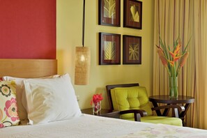 Een hotelkamer met een bed, een stoel, een tafeltje en een vaas met bloemen.