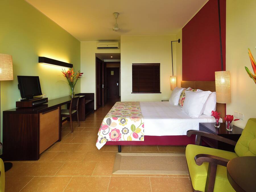 Quarto de hotel com cama, escrivaninha, cadeira e televisão.