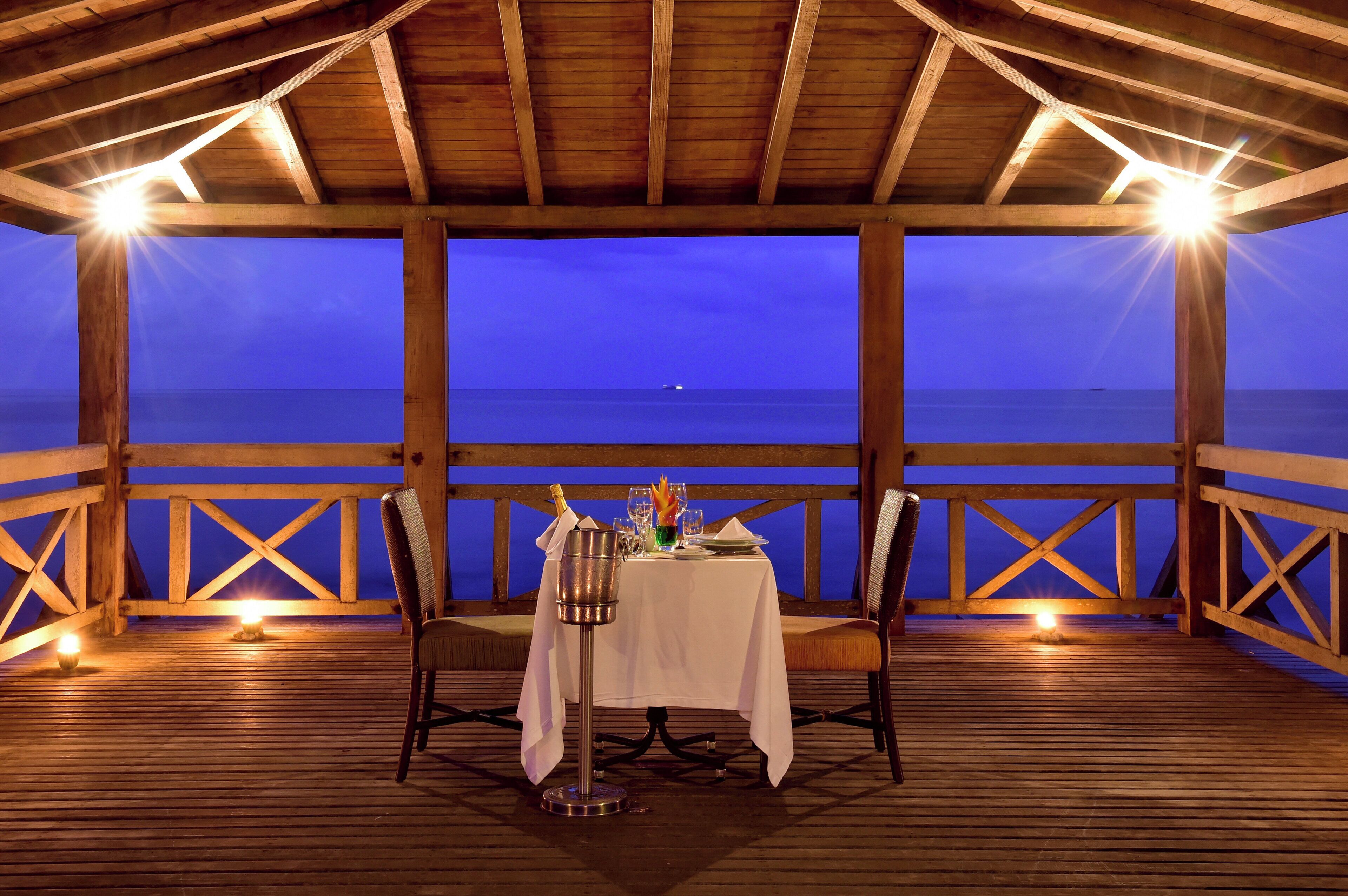 An outdoor dining area with a table set for two, overlooking a body of water.
