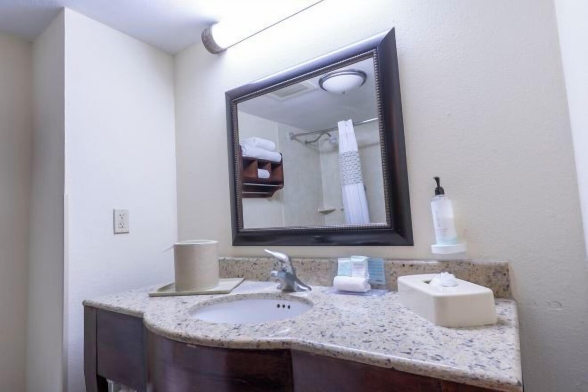A bathroom with a granite countertop sink, a mirror, a towel rack, and a soap dispenser.
