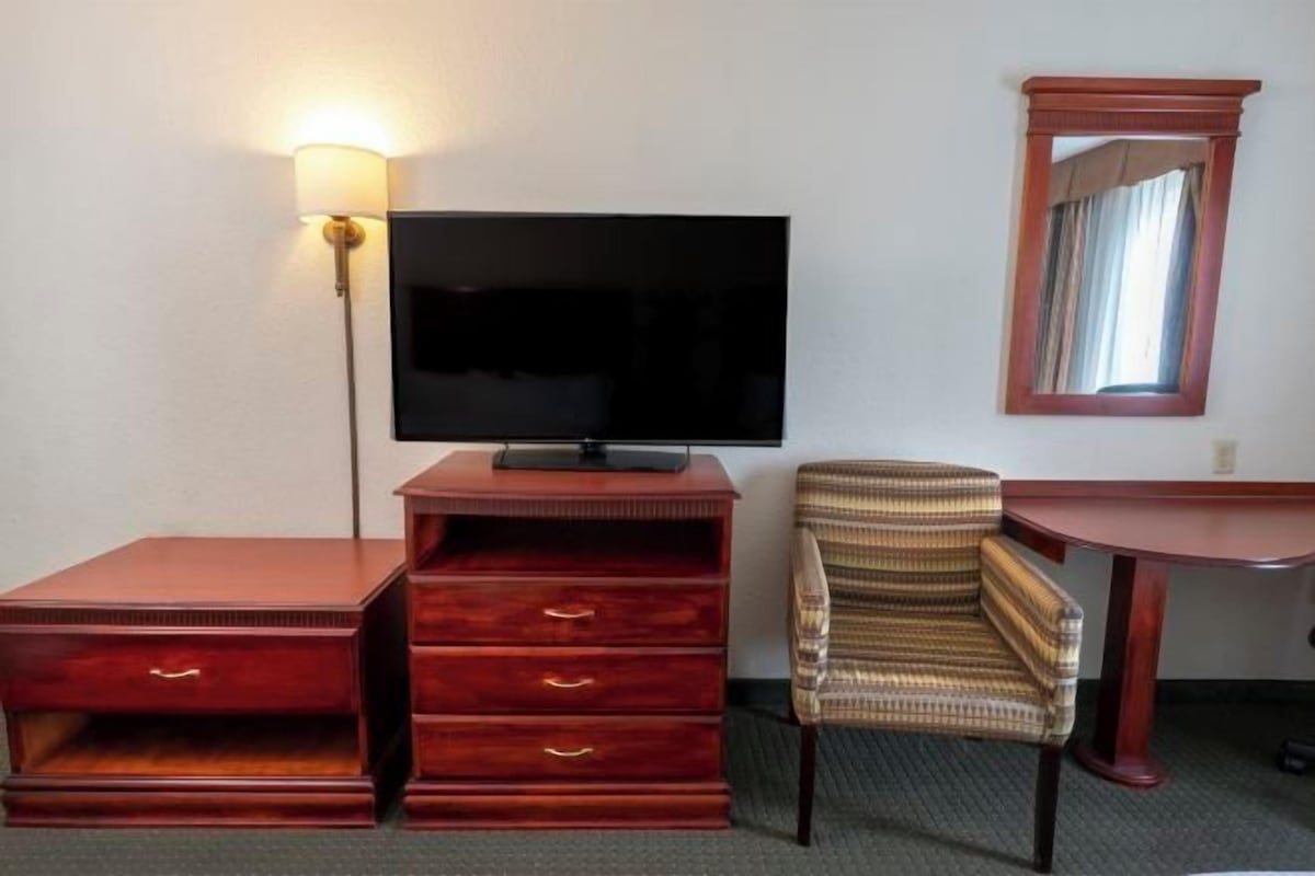 Une chambre d’hôtel avec une télévision, une commode en bois, un fauteuil à rayures et une petite table.