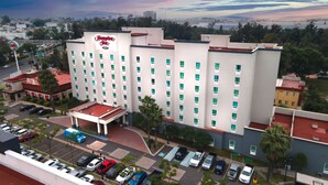 A Hampton Inn hotel with a central courtyard, parking lot, and a view of the surrounding cityscape. - Hampton Inn by Hilton Guadalajara-Aeropuerto (El Salto)