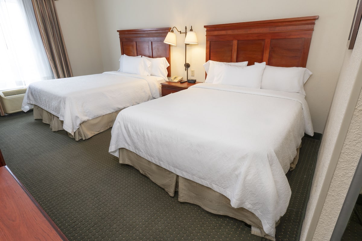 Une chambre d’hôtel avec deux lits simples, une tête de lit en bois, une table de chevet avec une lampe et un sol recouvert de moquette.
