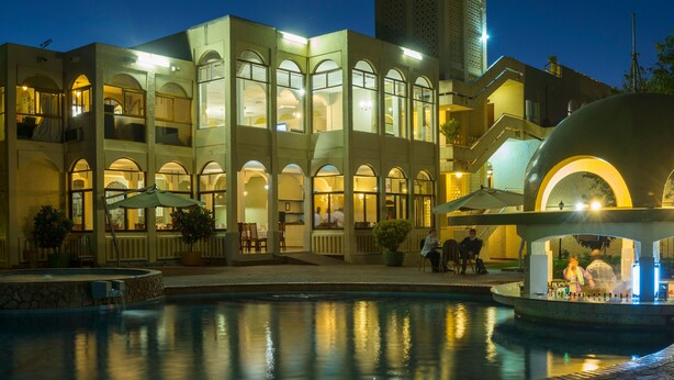 Un hotel con piscina, mobiliario exterior y una amplia entrada en arco.