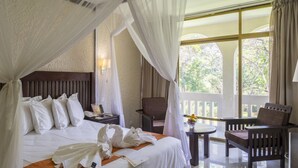 Habitación de hotel con cama, una silla, una mesita y balcón con vista a árboles.