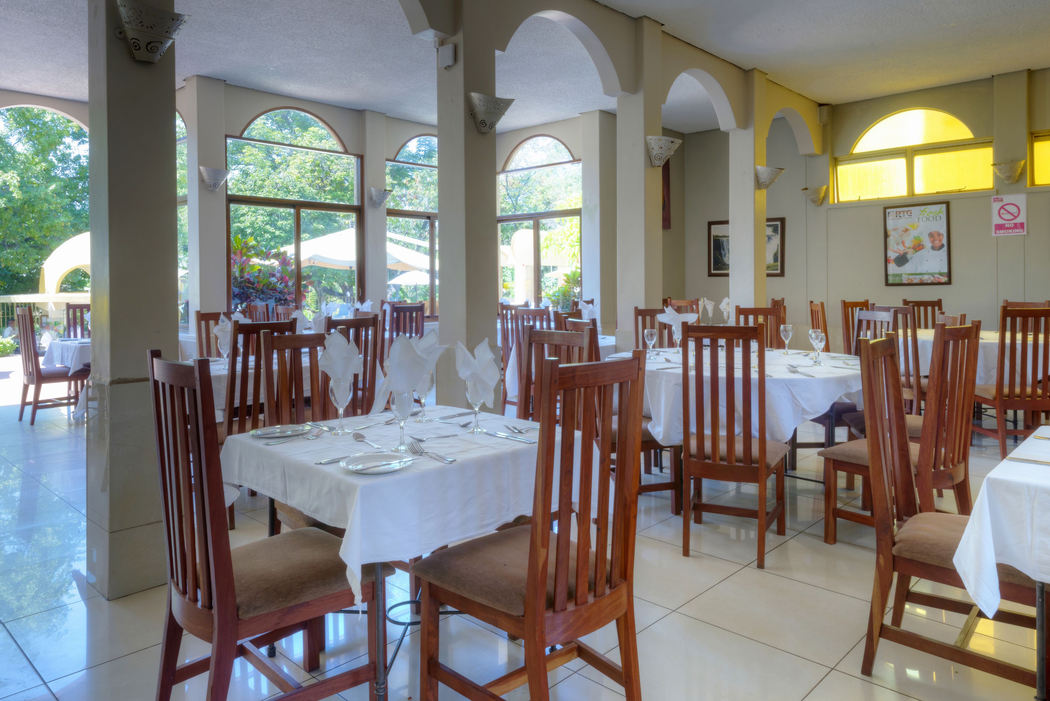 A restaurant with multiple tables and chairs, large windows, and a tiled floor.