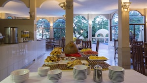 Montaje de bufé con distintos alimentos y platos, una cafetera y un gran jarrón decorativo.